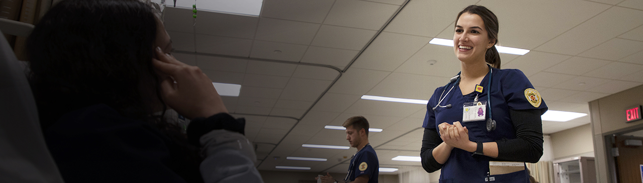 Female nursing student in scrubs talks to a patient