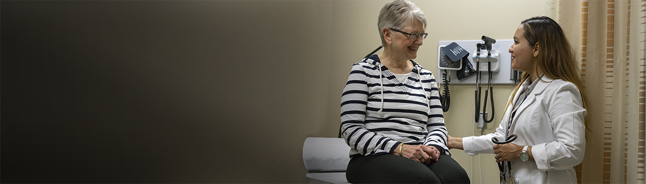 Female nurse in white coat talks to an adult patient in a hospital room
