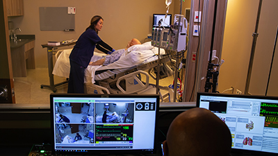 Woman works on a dummy in the Clinical Learning Center while man on computer watches