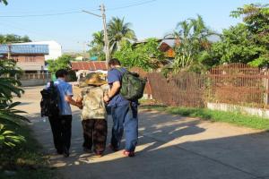 Two men walk an elderly woman down the road.