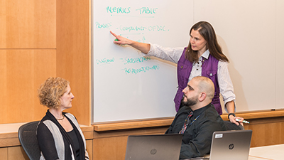 Professor points to a whiteboard to show two students an example