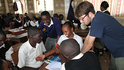 Student teaches children in Africa about nursing around a table. 