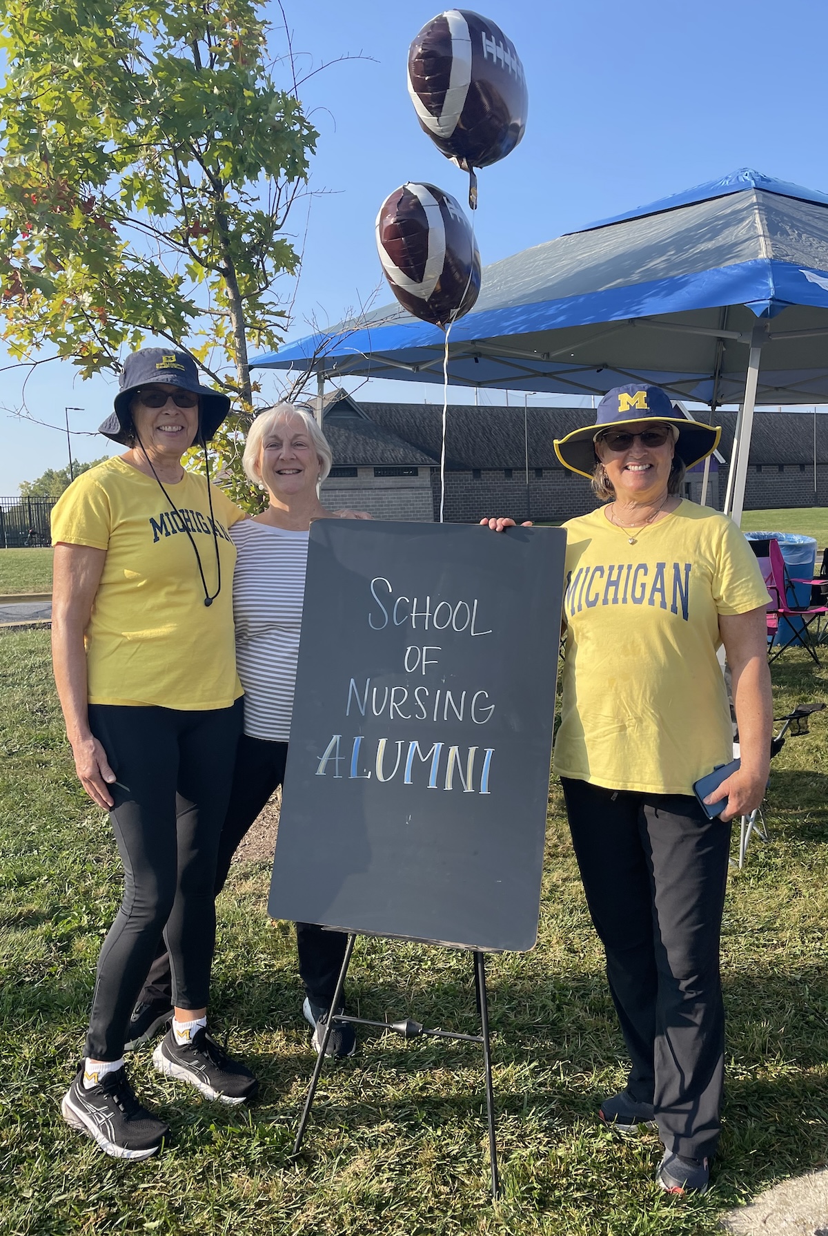 3 alumni standing next to a sign that reads "School of Nursing Alumni"