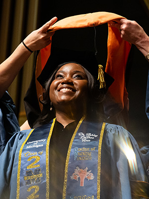 Student smiling at graduation ceremony as a sole is draped over her sholulders