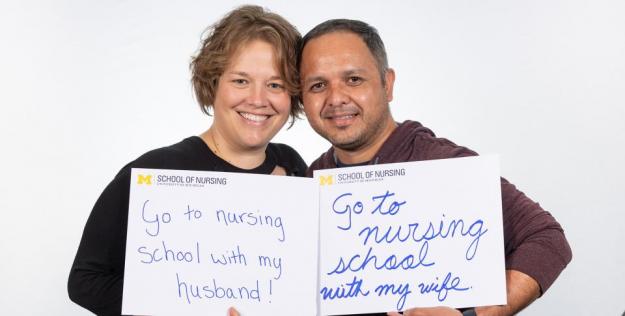 Eddie and Tamara Villavicencio hold signs that say "go to nursing school with my wife"