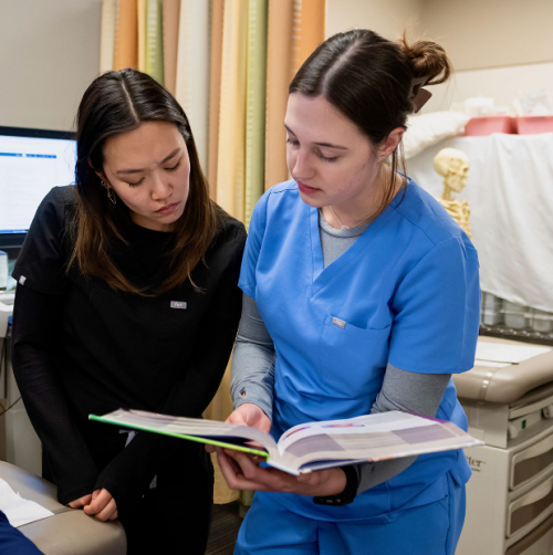 Two female nursing students attentively studying a book together, deep in thought and focused on their task. 