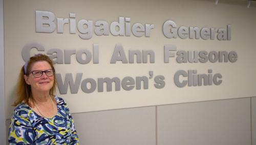 Brigadier General Carol Ann Fausone standing in front of a sign for a women's clinic renamed in her honor.